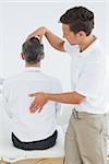 Rear view of a male chiropractor examining mature man at office