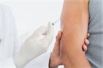 Close-up mid section of a male doctor injecting a patients arm over white background