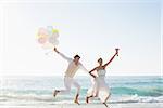 Newlyweds having fun holding balloons at the beach