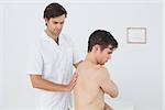 Side view of a shirtless man being massaged by a physiotherapist over white background