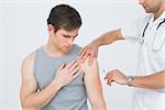 Male doctor injecting a young male patients arm over white background