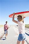 Couple carrying surfboard on coastal path, Breezy Point, Queens, New York, USA