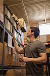 Worker looking at cardboard boxes on shelves in warehouse