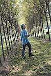 A man walking down an avenue of trees, looking upwards.