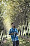 A man standing in an avenue of trees, holding a digital tablet.