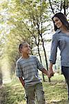 A woman and a young boy holding hands, walking in woods.