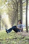 A woman sitting reading a book under the trees.