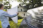 A man using a plan to place a solar panel in a farmhouse garden.