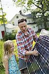 A man and a young girl looking at a solar panel in a garden.