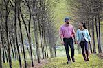 A couple walking between two rows of trees.