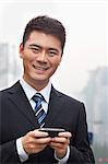 Young Businessman Smiling and Using a Smart Phone, Looking at Camera