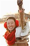 Young Woman Holding Up Ice Skates Outside, Beijing