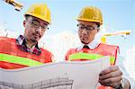 Two architects looking at a blueprint outdoors at a construction site