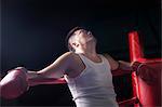 Tired boxer resting on the ropes in boxing ring, looking up