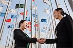 Two businesswomen shaking hands with flags in background.