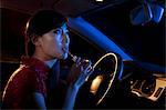 Young beautiful woman in traditional Chinese dress putting on lipstick in the rear view mirror of the car at night