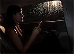 Young woman sitting in the car and texting on her phone on a rainy night in Beijing