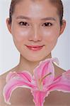 Portrait of young tranquil woman looking at camera with a large pink flower, studio shot