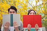 Young happy couple sitting side by side and reading their books, face partially obstructed, outdoors in springtime