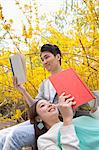 Young happy couple lying and sitting on a park bench enjoying reading their books, outdoors in springtime