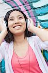 Young smiling woman holding her headphones while enjoying listening to music in front of wall with graffiti
