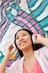 Young smiling woman holding her headphones while enjoying listening to music in front of wall with graffiti