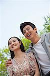 Smiling happy young couple with arm around the shoulders outdoors in a park, front view