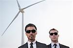 Portrait of two serious young businessmen in sunglasses standing by a wind turbine