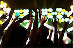 Audience watching a rock show, hands in the air, rear view, stage lights
