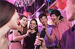 Group of friends holding microphones in a nightclub and singing together karaoke