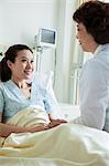 Female doctor sitting on hospital bed and discussing with young female patient