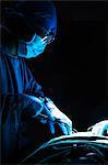 Surgeon looking down, working, and holding surgical equipment with patient lying on the operating table