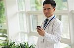 Smiling doctor looking down at his phone in the hospital lobby