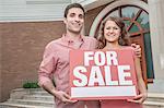 Smiling young couple holding a For Sale sign