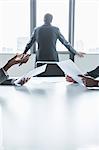 Two business people discussing and gesturing over the table while another looks out the window, hands only