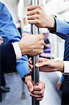 Close-up of four business people's hands holding the pole on the subway