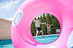 Father and daughter holding hands and jumping into the pool, seen through an inflatable pink tube