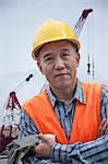 Portrait of proud worker with arms crossed in protective workwear outside in a shipping yard, crane in the background