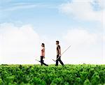 Two young people carrying gardening equipment walking across a green field with plants