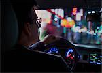 Over the shoulder view of businessman driving at night in the city, illuminated city lights