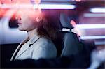 Serene businesswoman sitting in the car at night, illuminated and reflected lights on the car window