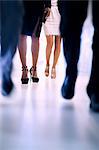 Low view of people walking down the corridor in an office building, focus on high heels