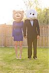 Portrait of couple standing in backyard dressed in formal attire, covering faces wearing costume bear heads, Canada