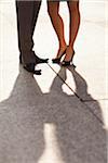 Close-up of young couples legs and feet with shadows, wearing dress shoes and standing on sidewalk, Canada