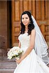 Close-up portrait of Bride in wedding gown holding bridal bouquet, standing on stairs in front of building, smiling and looking at camera on Wedding Day, Canada
