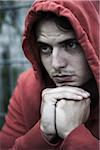 Close-up portrait of young man outdoors wearing red hoodie, looking upset, Germany