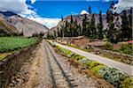 Train rails next to rural homes and farmland on scenic journey through the Sacred Valley of the Incas in the Andes mountains, Peru