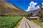 Train rails next to rural homes and farmland on scenic journey through the Sacred Valley of the Incas in the Andes mountains, Peru