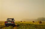 Car driving through field of haystacks on overcast day