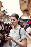 Young woman texting on cell phone, San Lorenzo market, Florence, Tuscany, Italy